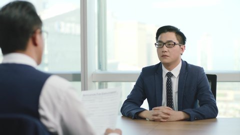 young asian business man being interviewed by HR manager in office of modern corporation, zooming out