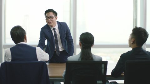 young asian business man job applicant shaking hands with and greeting a group of human resources executives in conference room of modern corporation