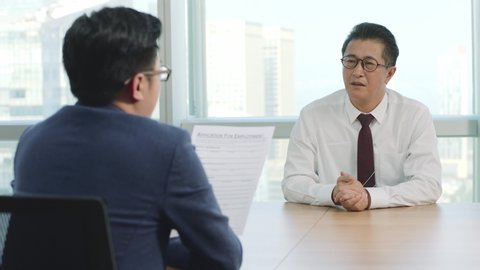 nervous mature asian business man being questioned by HR manager during job interview