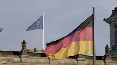 Slo motion clip of massive German flag flying in front of EU flag over the Reichstag Building in Berlin with slow zoom in