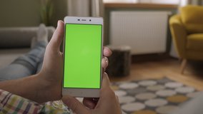 Young Woman Home Lying on a Couch with Green Screen Smartphone in Vertical Mode. Girl Using Touchscreen Mobile Phone. Woman Using Smartphone, Browsing Internet, Watching Video Content, Blogs. POV.