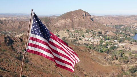 American Flag blowing in the wind with mountains landscape and blue sky on a background. USA American Flag. Waving United states of America famous flag in front of green suburban. American concept.