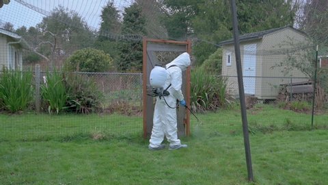 Man wearing protective gear spraying weed killer in yard