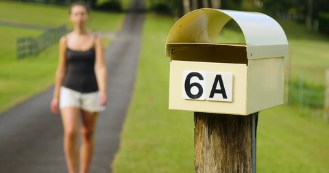 Young woman collects post from outdoor mailbox