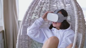 Pretty Young Woman in Hanging Chair is Having VR Experience. Pretty caucasian lady wearing vr goggles feel fear, excited and amazed of watching movie vr content 360.