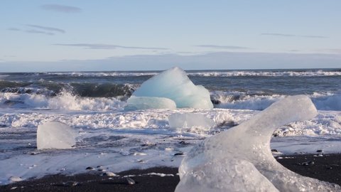 Waves crash against huge pyramid- shaped chunk of ice in slow motion at Diamond Beach in Iceland.