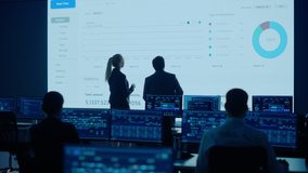 Project Leader and Chief Executive Discuss Data Shown on Big Display. Screens Show Infographics, Charts, Finance Analysis, Stock Market, Growth. Telecommunications System Control Room - Powered by Shutterstock - Get 15% off with code: PIKWIZARD15