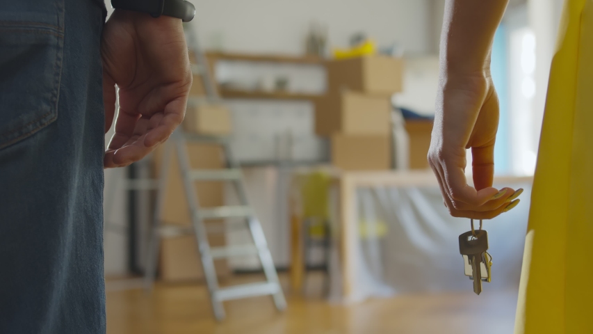 Close up of couple holding hands and keys to new apartment over background with boxes. Happy young family buying or renting new house and moving in together | Shutterstock HD Video #1056222965