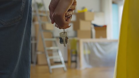 Close up of couple holding hands and keys to new apartment over background with boxes. Happy young family buying or renting new house and moving in together