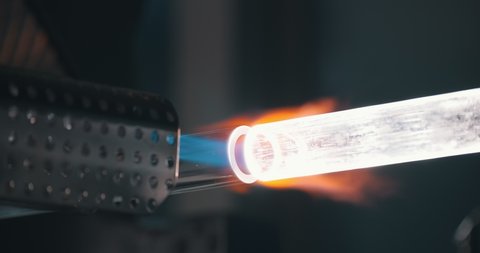 Close up of torch melting glass or plastic pipe on manufacturing plant. Industrial worker blowing glass tube with flame at factory. Optic fibre and glassblowing industry concept