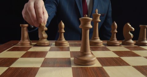 Close up of businessman moving white knight on chessboard isolated on black background. Grandmaster making strategic move with horse during chess tournament. Intelligence and tactic concept