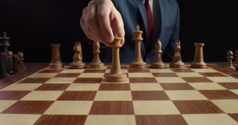 Close up of businessman hand moving white queen piece on chess board isolated over black background. Man playing chess game. Leadership, and business strategy concept