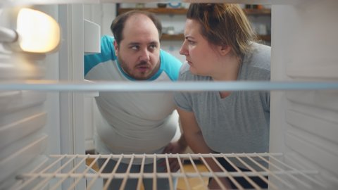 Overweight young couple on diet looking in empty fridge. Hungry obese man and woman keeping weight loss diet looking for food in empty refrigerator