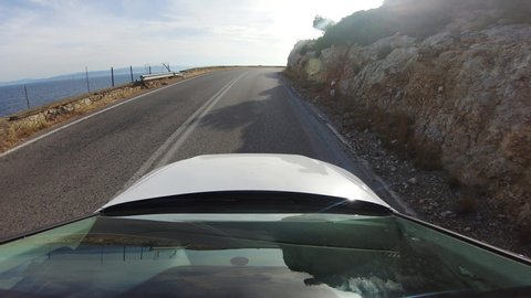 Beautiful Driver POV on a coastal road of the Corinthian golf in Greece with bright sunlight shine in the seawater. Reflective windshield view.
