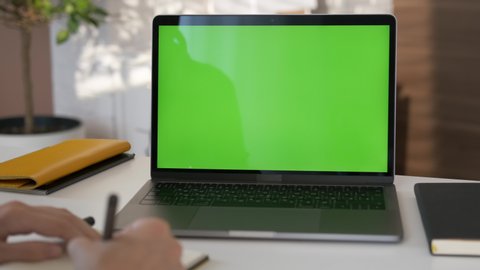Girl looking at green screen laptop computer in living room watching movie, video content. Business woman or female freelancer working from home office. 
