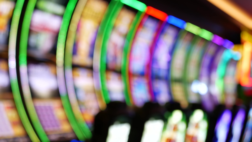 Defocused slot machines glow in casino on fabulous Las Vegas Strip, USA. Blurred gambling jackpot slots in hotel near Fremont street. Illuminated neon fruit machine for risk money playing and betting. Royalty-Free Stock Footage #1056229199