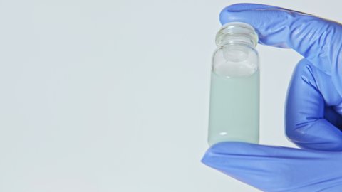 Drug sample. Pharmaceutical test. Hand in blue glove holding liquid solution in glass bottle isolated on white loop.