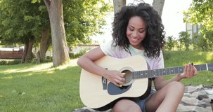 Smiling african american woman playing acoustic guitar on plaid in park