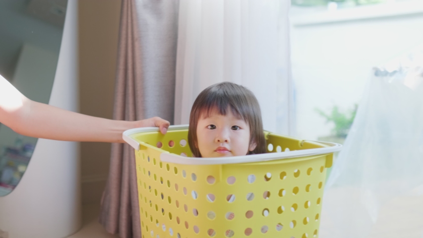 Asian little baby girl sit in big basket was push by mother and slide around in warm house. Girl smiling and feeling happy to play with mom at home. Kid activity and education lifestyle concept.