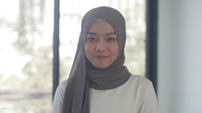 Portrait of successful beautiful executive businesswoman casual wear looking at camera and smile, happy in modern office workplace. Young Asia muslim lady stand relax in contemporary coworking space. | Shutterstock HD Video #1056232652
