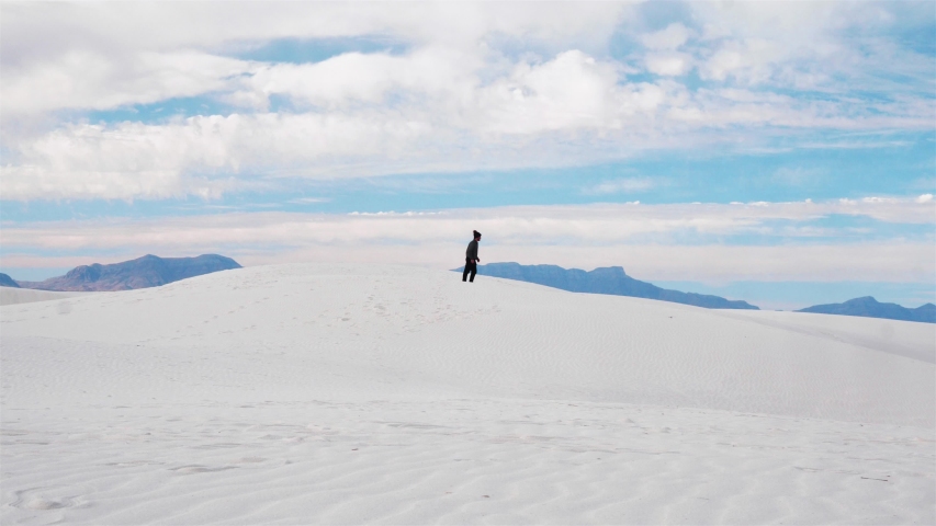 Slow motion shot of a man running and jumping off of a large sand dune in the famous White Sands national monument park in New Mexico on a bright sunny summer day.