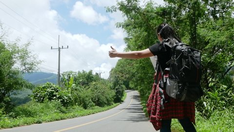 Travel woman backpacking hitchhiking by the road during summer vacation trip in amazing landscape nature in Thailand. Traveling and hitchhiking concepts.