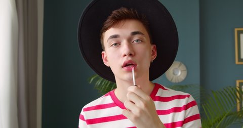 Young man queer doing makeup lipstick or lip gloss and paints lips prepare getting ready looking in camera like mirror. Beauty blogger hipster makes a makeup tutorial video. : vidéo de stock