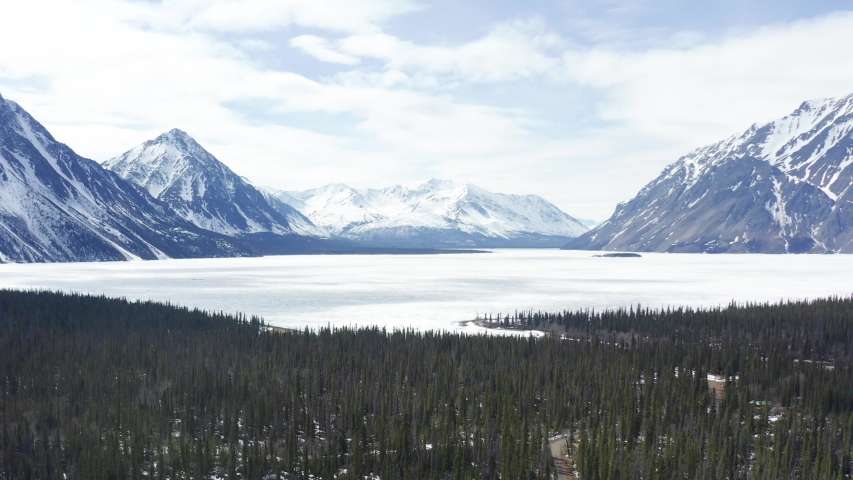 Aerial shot of Frozen Kathleen Lake with the thawing Kathleen River in the foreground. Taken on a sunny day in spring in the Yukon. Royalty-Free Stock Footage #1056237419