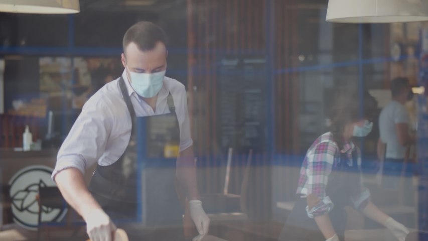 View through window of team waiters in facial mask closing cafe because of quarantine. Restaurant staff cleaning and arranging furniture after closing in evening. Small business and pandemic concept | Shutterstock HD Video #1056238487