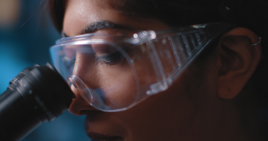 Close up of a female research scientist eyes, looking at samples under microscope, wearing safety glasses.Slow motion, slider, shot with BMPCC 4K.Biochemistry, pharmaceutical medicine,science
