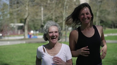 Cheerful old and young women enjoying running together in park, talking and laughing. Medium shot, front view, dolly. Friendship and outdoor activity concept
