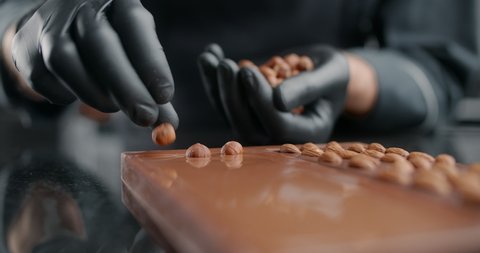 Confectioner adds roasted hazelnuts to the hot handmade chocolate bar, the art of chocolate, cooking desserts from chocolate and cocoa, making bars, sweet desserts, 4k 120 fps Prores HQ