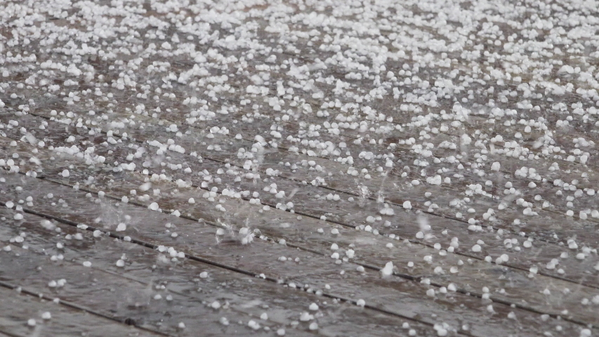 Very intensive summer hail storm on wet wooden terrace covered by white round frozen hailstones. Close up panning video. Unpredictable summer weather weather conditions. Original sound included