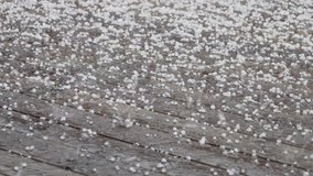 Very intensive summer hail storm on wet wooden terrace covered by white round frozen hailstones. Close up panning video. Unpredictable summer weather weather conditions. Original sound included