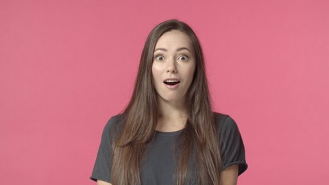 Surprised attractive caucasian brunette, looking camera casual normal face then see something intriguing, open eyes and smiling amused, cheerfully react, pink background