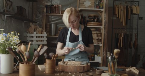 Woman carpenter polishes wooden spoon with a sandpaper