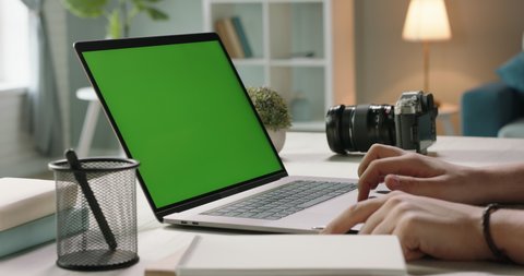 Close up shot of hands of student working with chroma key green screen laptop, using trackpad and pen with notebook in living room - technology concept 4k video template