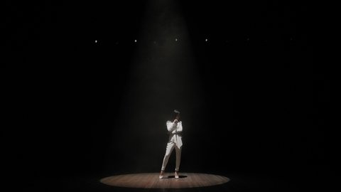 The silhouette of the singer in the dark on the stage under the light of a single white bright spotlight, the light is turned off and the stage is plunged into darkness. Slow motion.