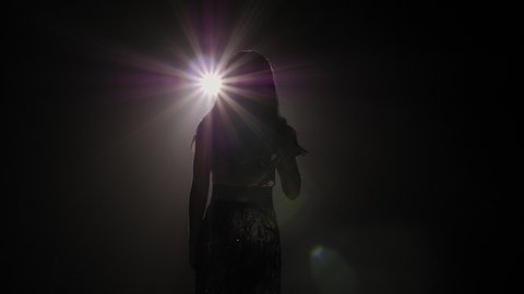 The silhouette of the singer in the dark on the stage under the light of a single white bright spotlight. Slow motion.