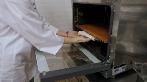 Close-up of the pastry chef takes out of the oven sponge dough, cake preparation. A woman in a chef's uniform is baking a cake in the oven. Slow motion.
