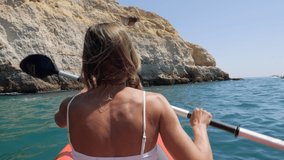 Rear view of woman paddling on red canoe in Portugal going trough rocky caves and cliffs.