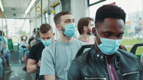 Multi-ethnic passengers in tram wearing protective face masks. Diverse people travel on public transport going to work during quarantine. Health care. Pandemic.