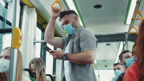Millennial guy in face mask using smartphone in the bus. All passengers having protective masks for safety. Health care measures. Covid-19 infection. Quarantine.
