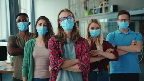 Multi-ethnic team of young ambitious employees wearing face masks, posing with crossing arms in the office. Coworking space. Business people. Corporate. Quarantine.