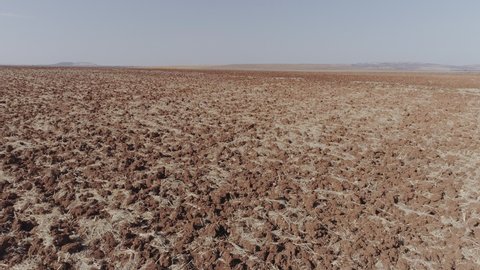 Aerial Drone fast close-up of dry plowed field and final upward movement with horizon and arid agricultural fields
