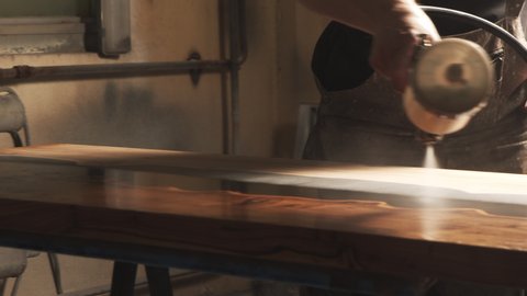 Close-up of a male carpenter's hands spraying varnish or primer using compressed air on a wooden tabletop. Furniture manufacture.