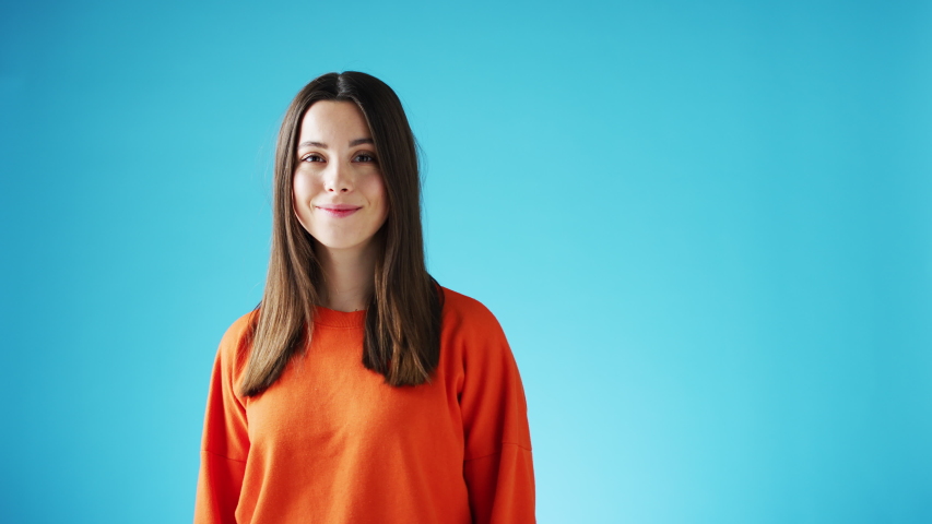 Studio portrait of confident smiling young woman laughing and celebrating against blue background - shot in slow motion Royalty-Free Stock Footage #1056266135