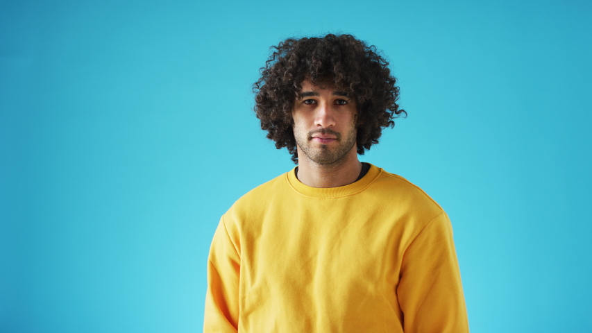 Studio portrait of young man whose expression and mood changes from serious to happy and laughing against blue background - shot in slow motion Royalty-Free Stock Footage #1056266147