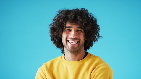 Studio portrait of confident smiling young man laughing against blue background - shot in slow motion
