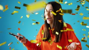 Celebrating young woman with mobile phone winning prize and showered with gold confetti in studio - shot in slow motion - Powered by Shutterstock - Get 15% off with code: PIKWIZARD15